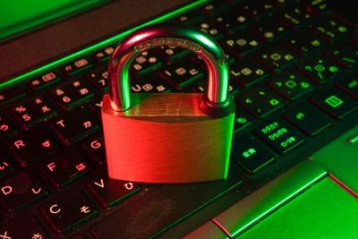 Ein geschlossenes Schloss auf einer Computer-Tastatur. Alles wird gespenstisch rot-grün angeleuchtet. Symbolbild für Cybersicherheit.